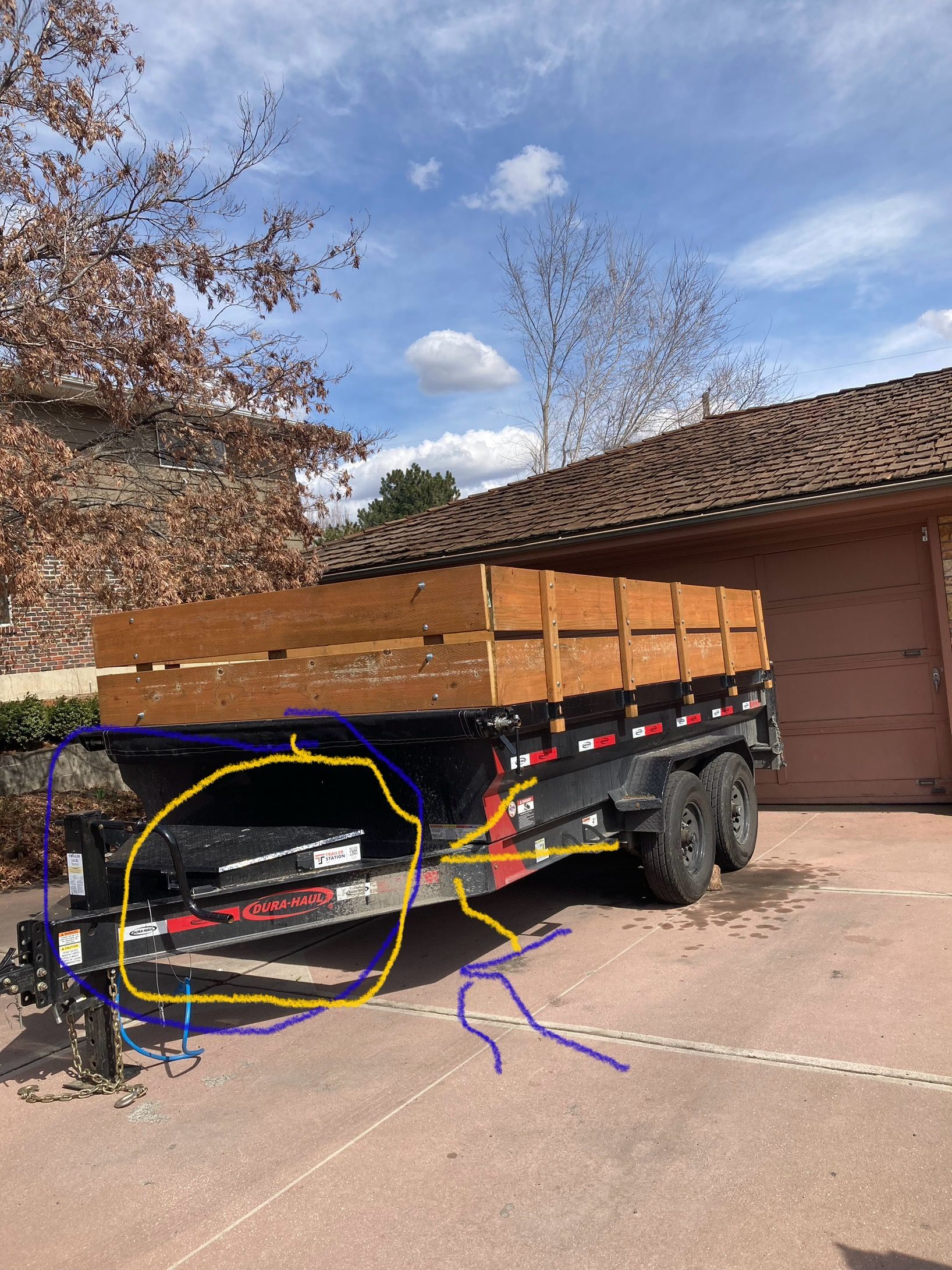 Flatbed trailer with wooden side panels parked in a driveway beside a brick garage.