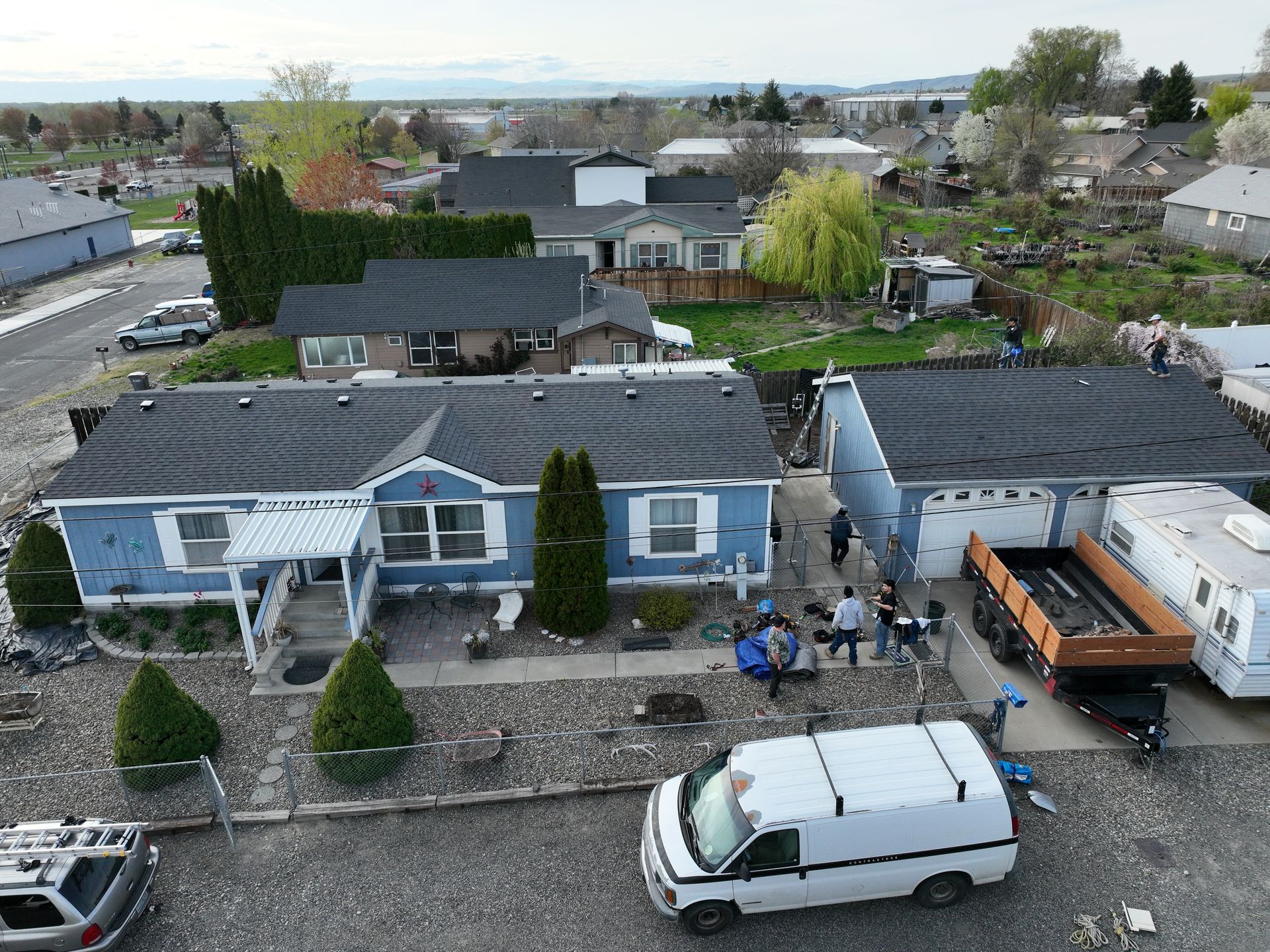 Aerial view of a suburban house with parked vehicles, a patio, and a fenced yard.