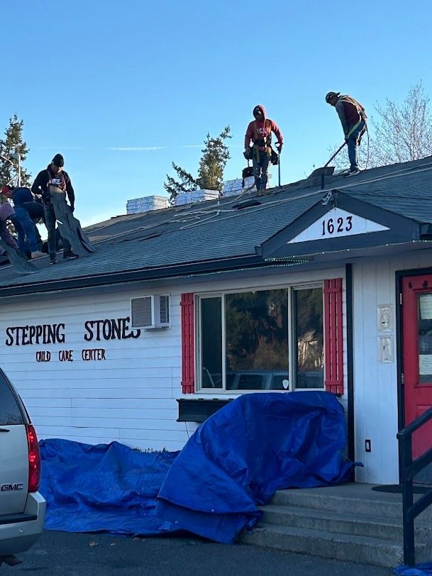 Workers on a roof above Stepping Stone Child Care, covering the building with blue tarps.
