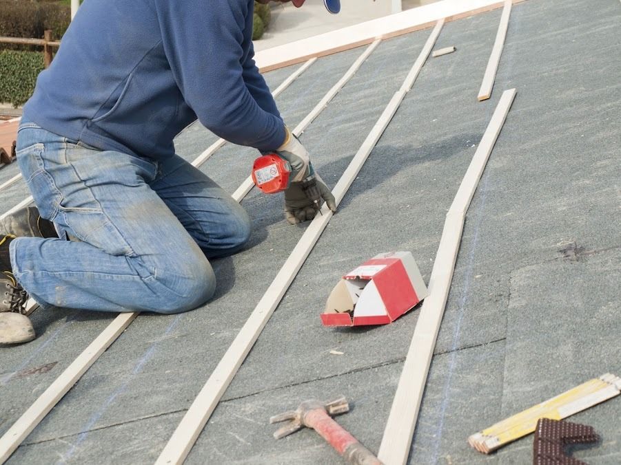 Worker kneeling on a rooftop, using a power tool to cut or install white trim pieces.