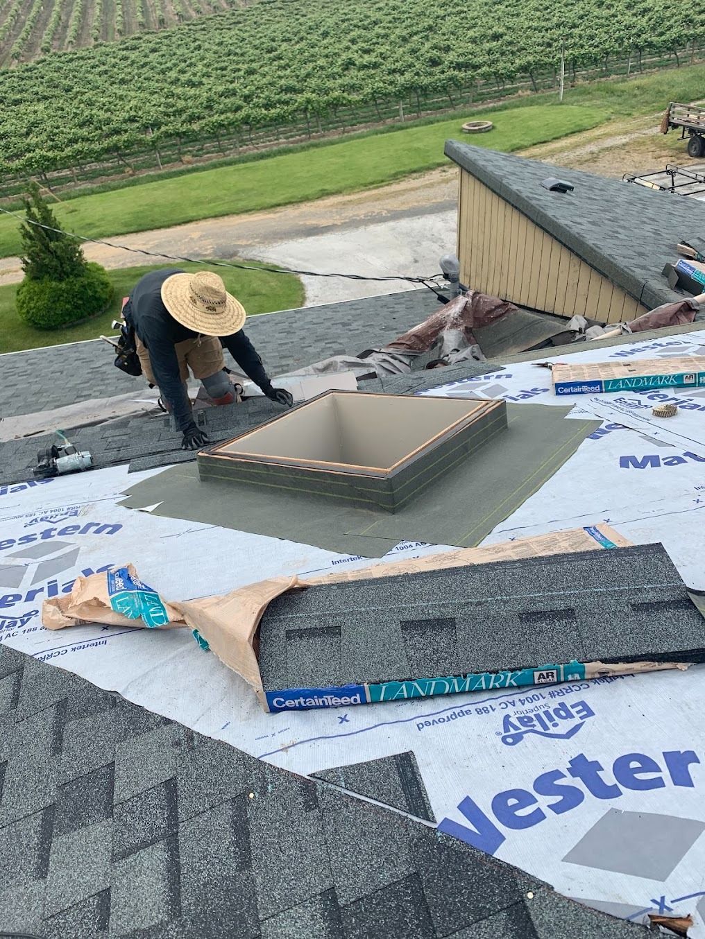 Worker installing roofing on a house with underlayment, vent opening, and stacked shingles nearby.