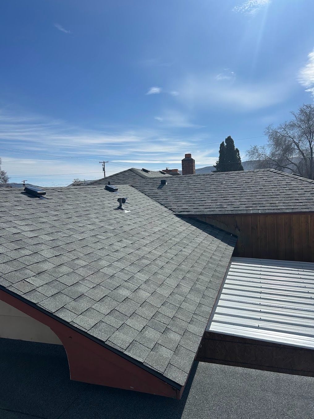 Gray shingled rooftops under a bright blue sky with a few clouds