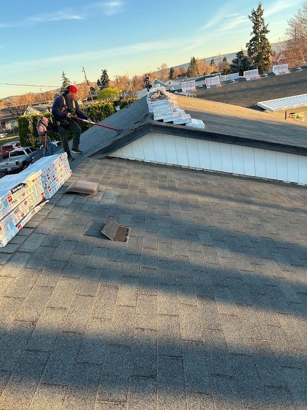 Worker on a sloped roof installing materials beside a white rooftop structure at sunset.