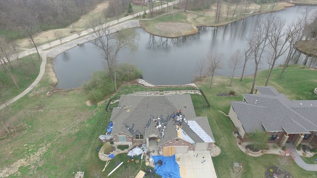 Aerial view of a pond beside two houses and a grassy yard with trees and a walkway