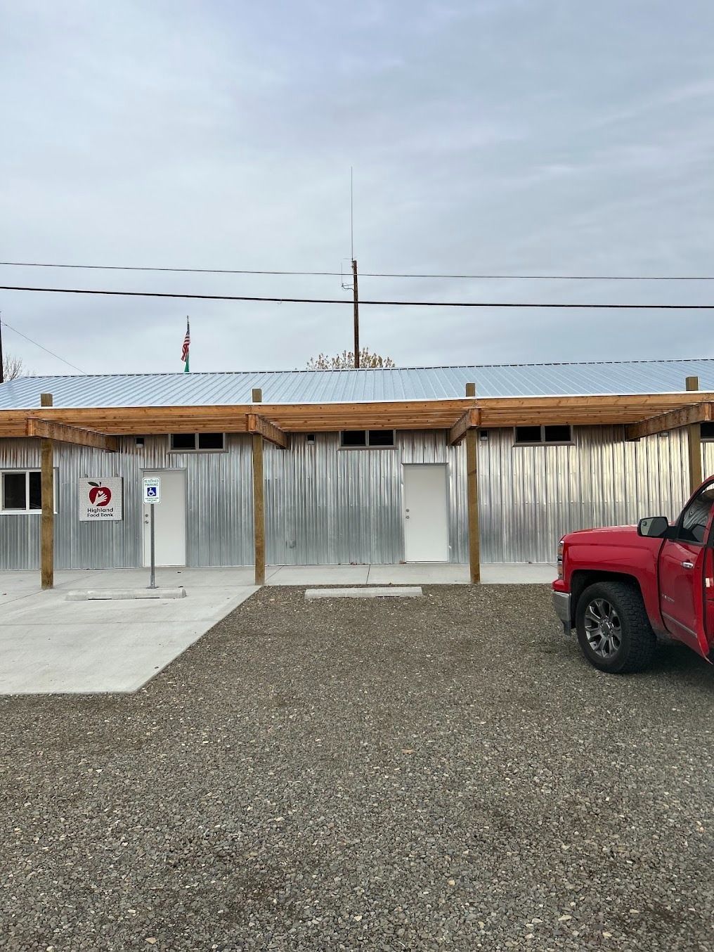 Metal building with a gravel lot and a red pickup truck parked on the right.