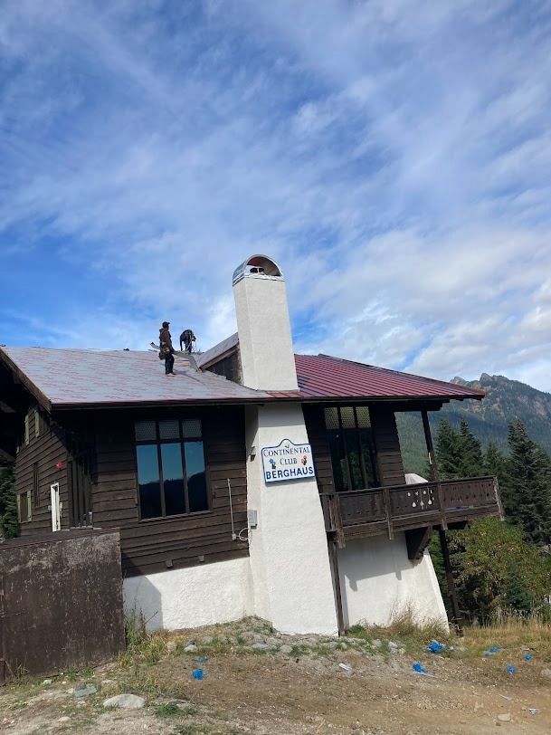 Rustic mountain house with a white chimney and red roof under a blue sky