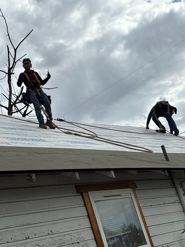 Two roofers on a sloped roof securing shingles under a cloudy sky
