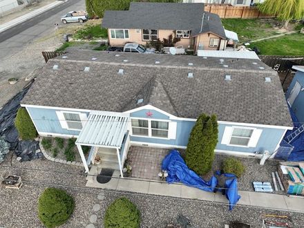 Aerial view of a blue house with a front porch, gravel yard, and blue tarp covering items near the entrance.