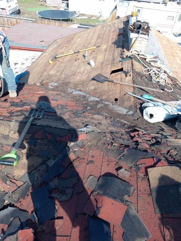 Damaged rooftop with torn shingles and debris, viewed from above on a sunny day.