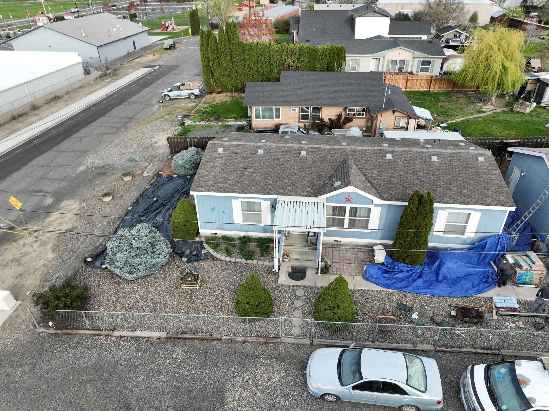 Aerial view of a small house with a gravel yard, parked car, and construction materials nearby