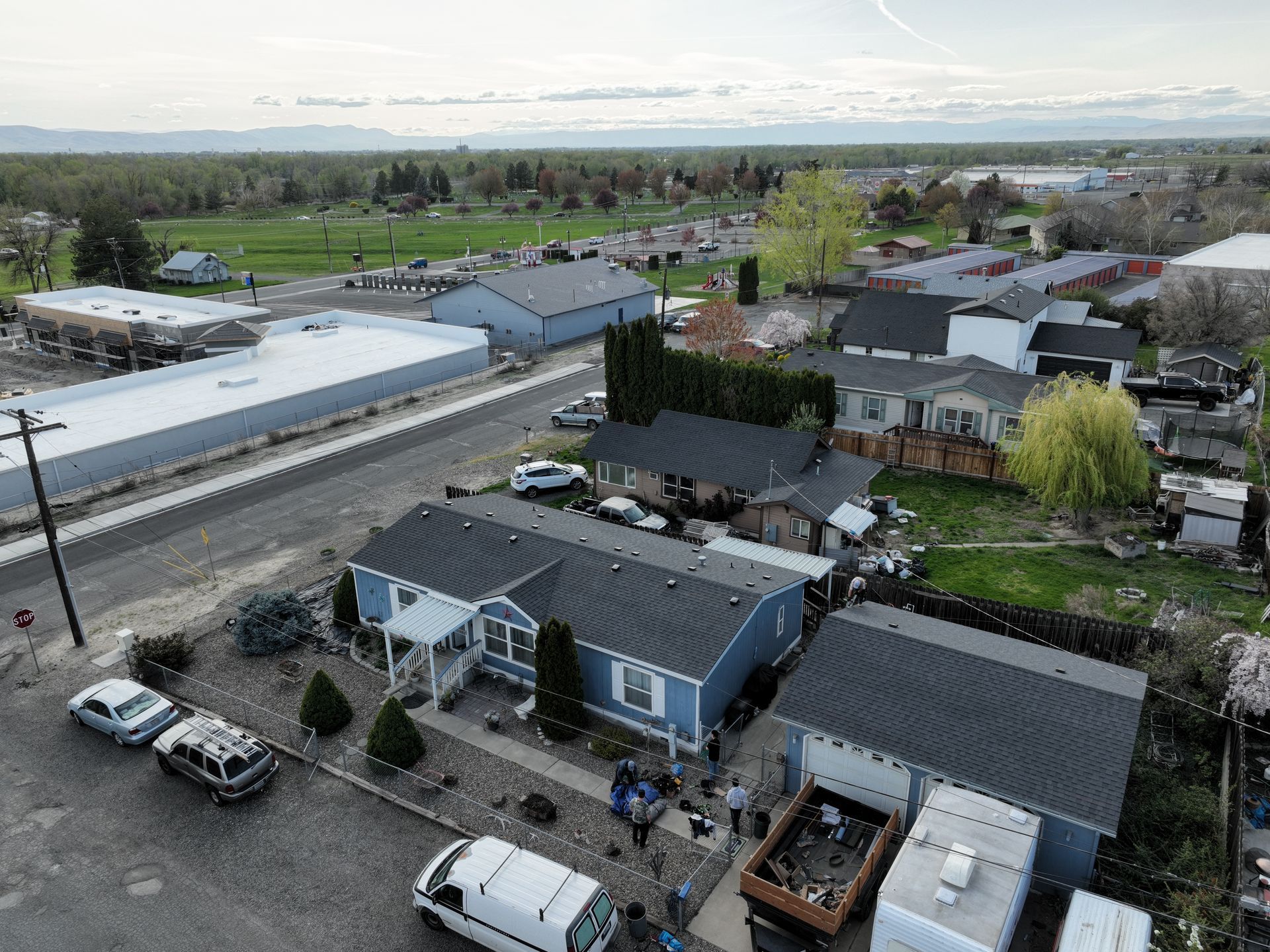 Aerial view of suburban homes, streets, and parked cars under a cloudy sky.