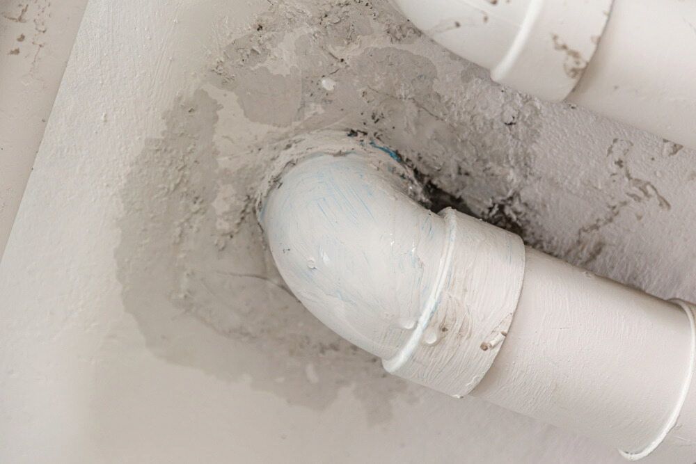 White Drain Pipe With a Leaking Joint and Water Stain on a Ceiling Above It — JAJ Plumbing in Mount Austin, NSW