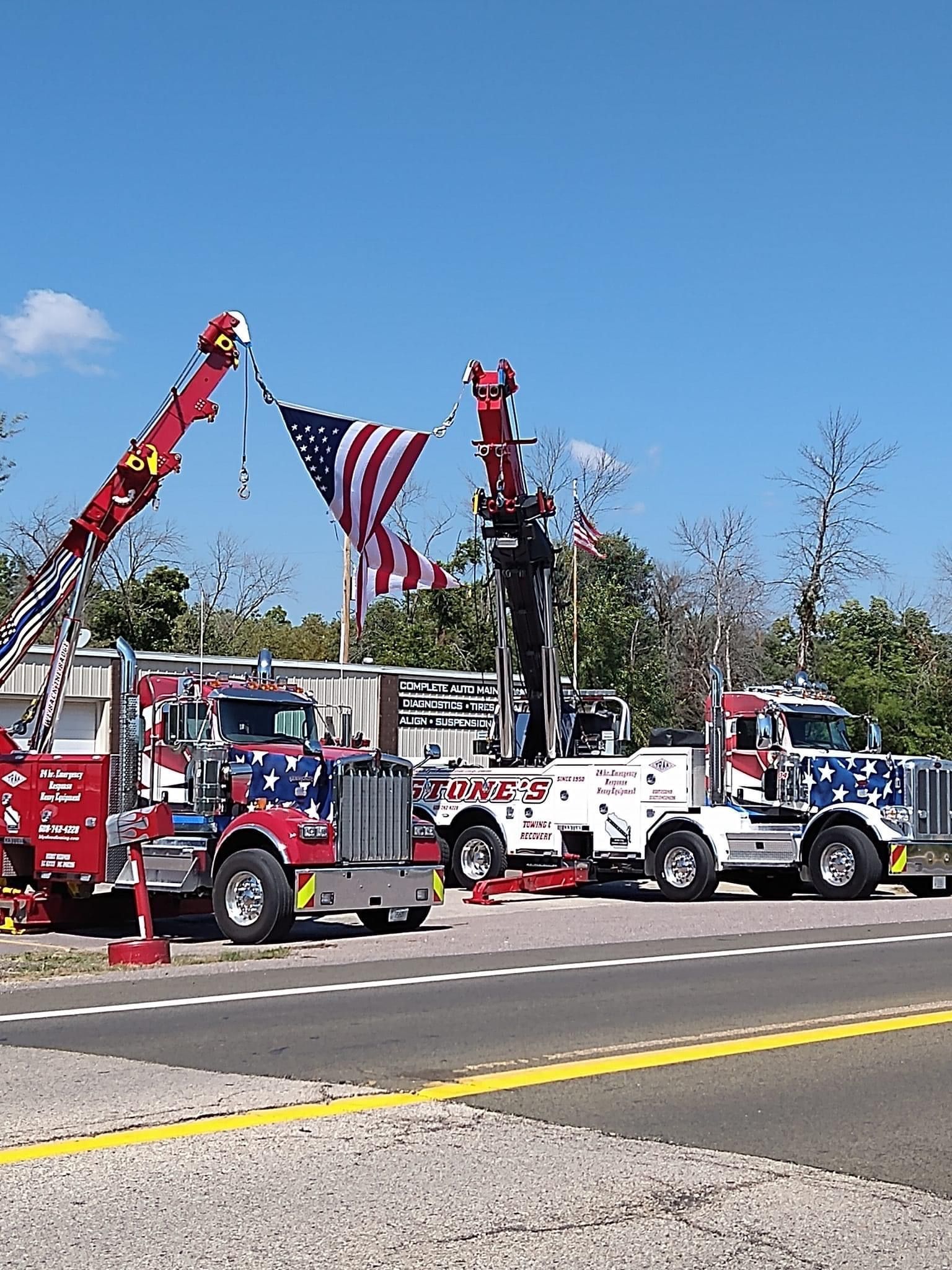 Tow trucks with American flag display against a bright blue sky, presumably at a patriotic event.