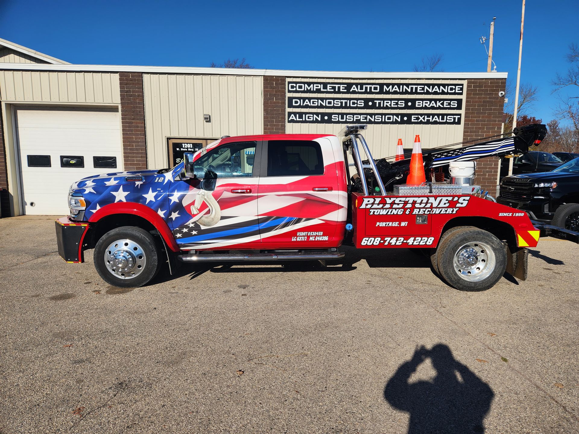 Tow truck with patriotic wrap in front of a garage.