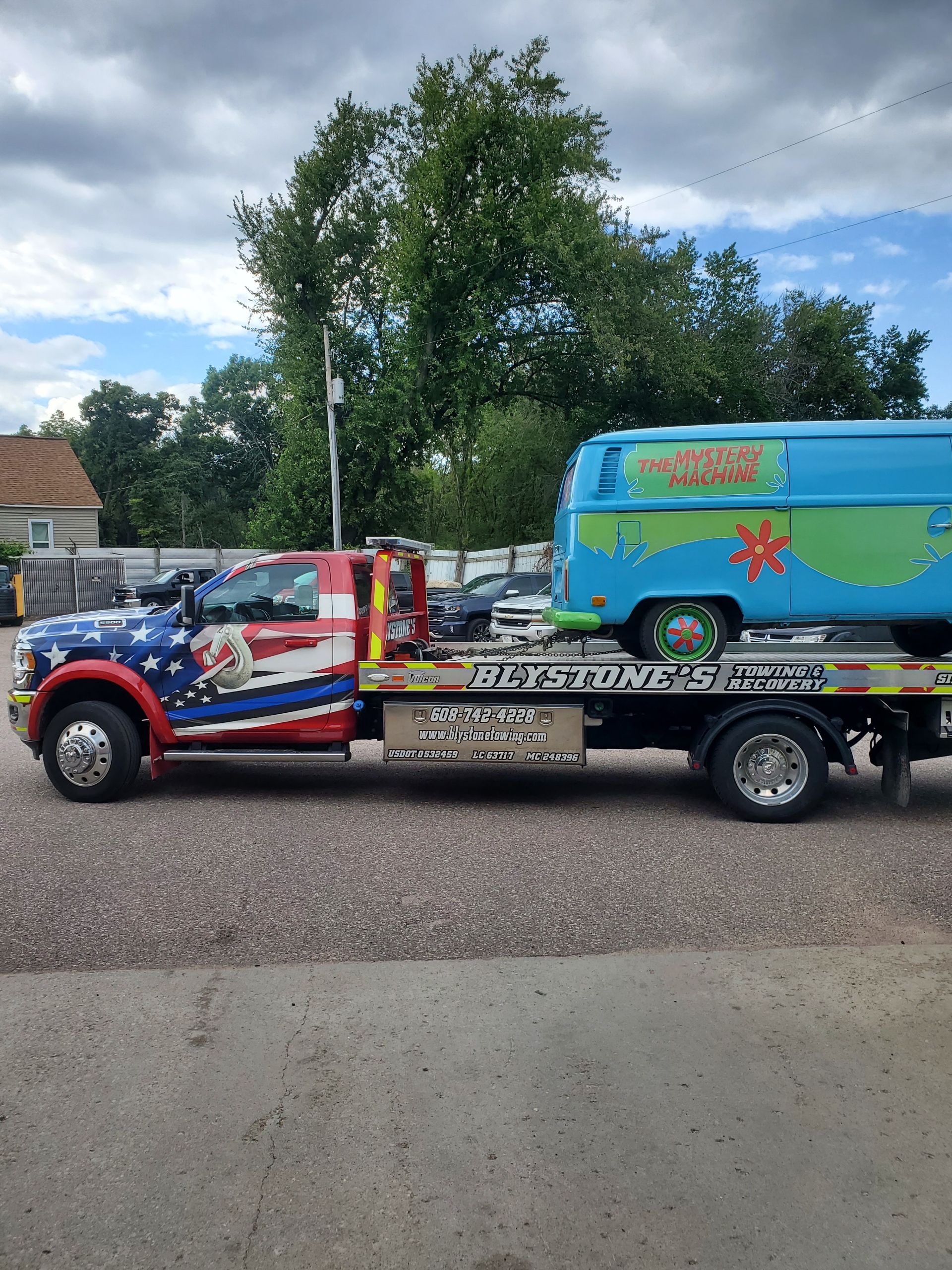 Tow truck with patriotic paint carrying the Mystery Machine van.