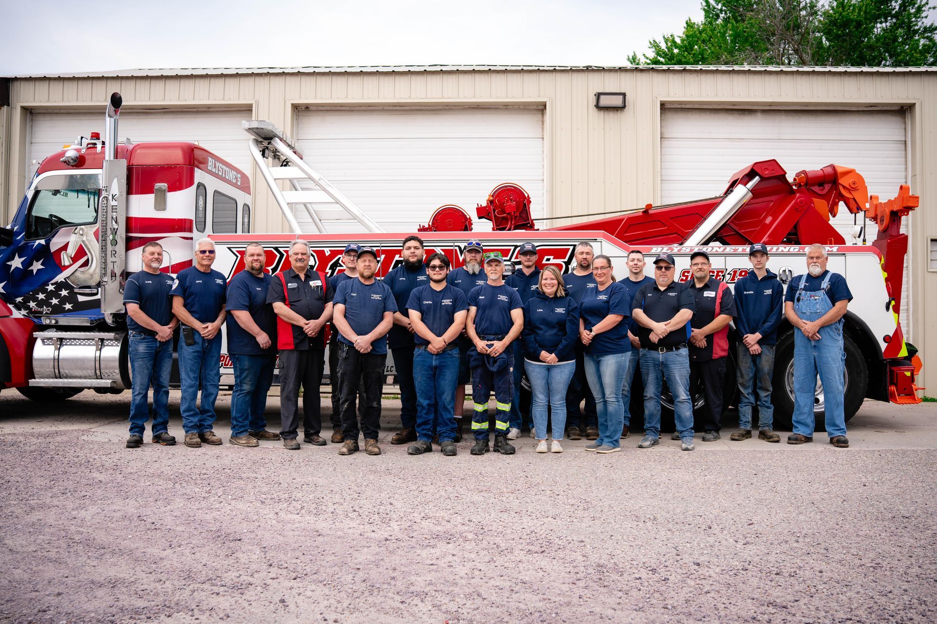 A group of people in blue shirts and jeans stand in front of a red and white tow truck.