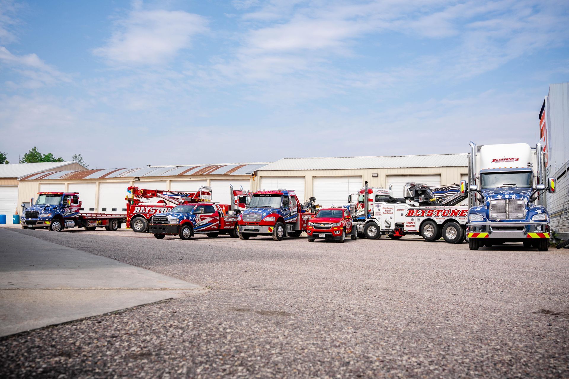 Several tow trucks of different sizes parked in front of a building on a sunny day.