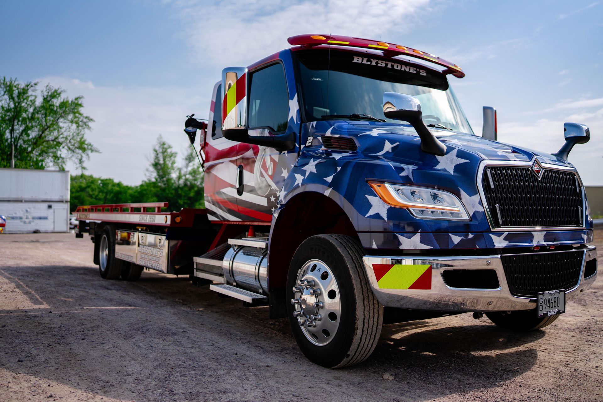 Tow truck with American flag design parked on gravel.