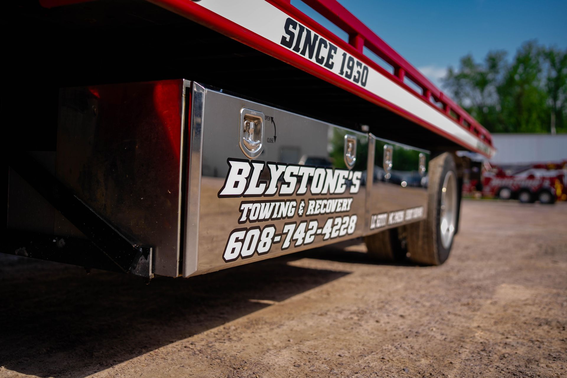 Blystone's Towing truck, logo on a side compartment. Silver and red, with the phone number 608-742-4228. 