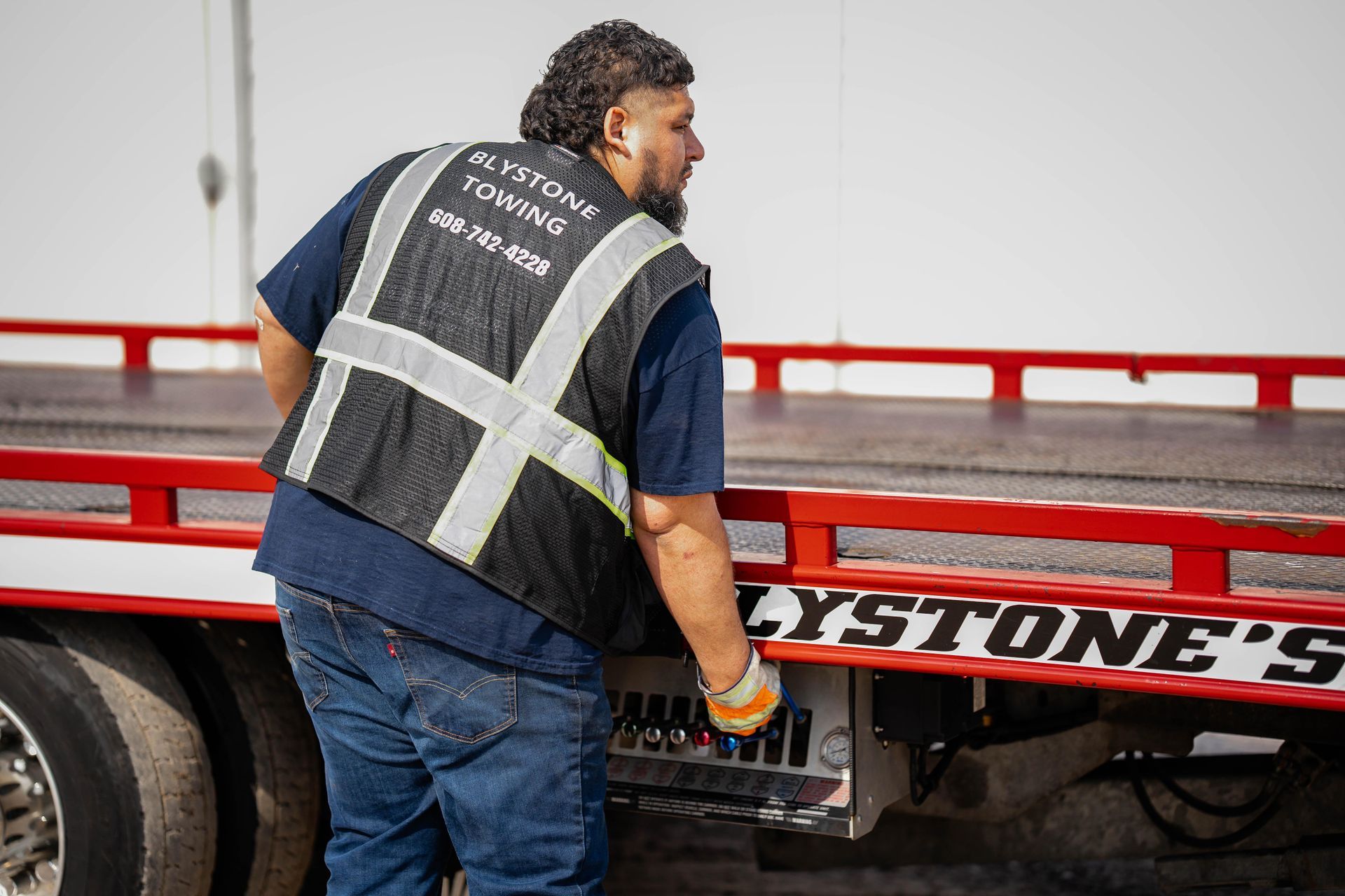 Man in reflective vest on a tow truck, preparing to load a vehicle.