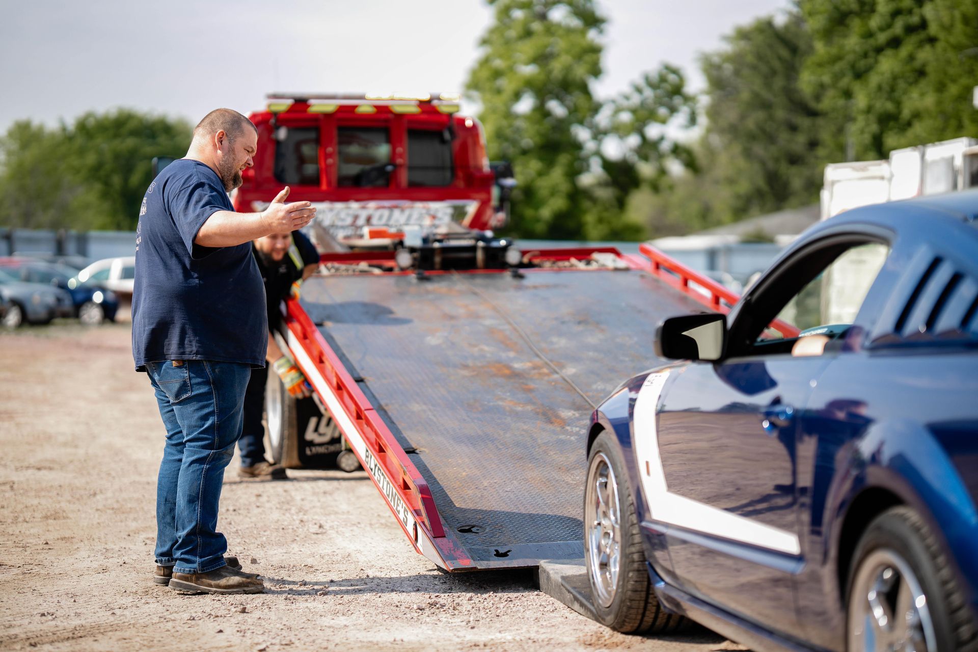 Man gesturing near a blue Mustang on a flatbed tow truck.