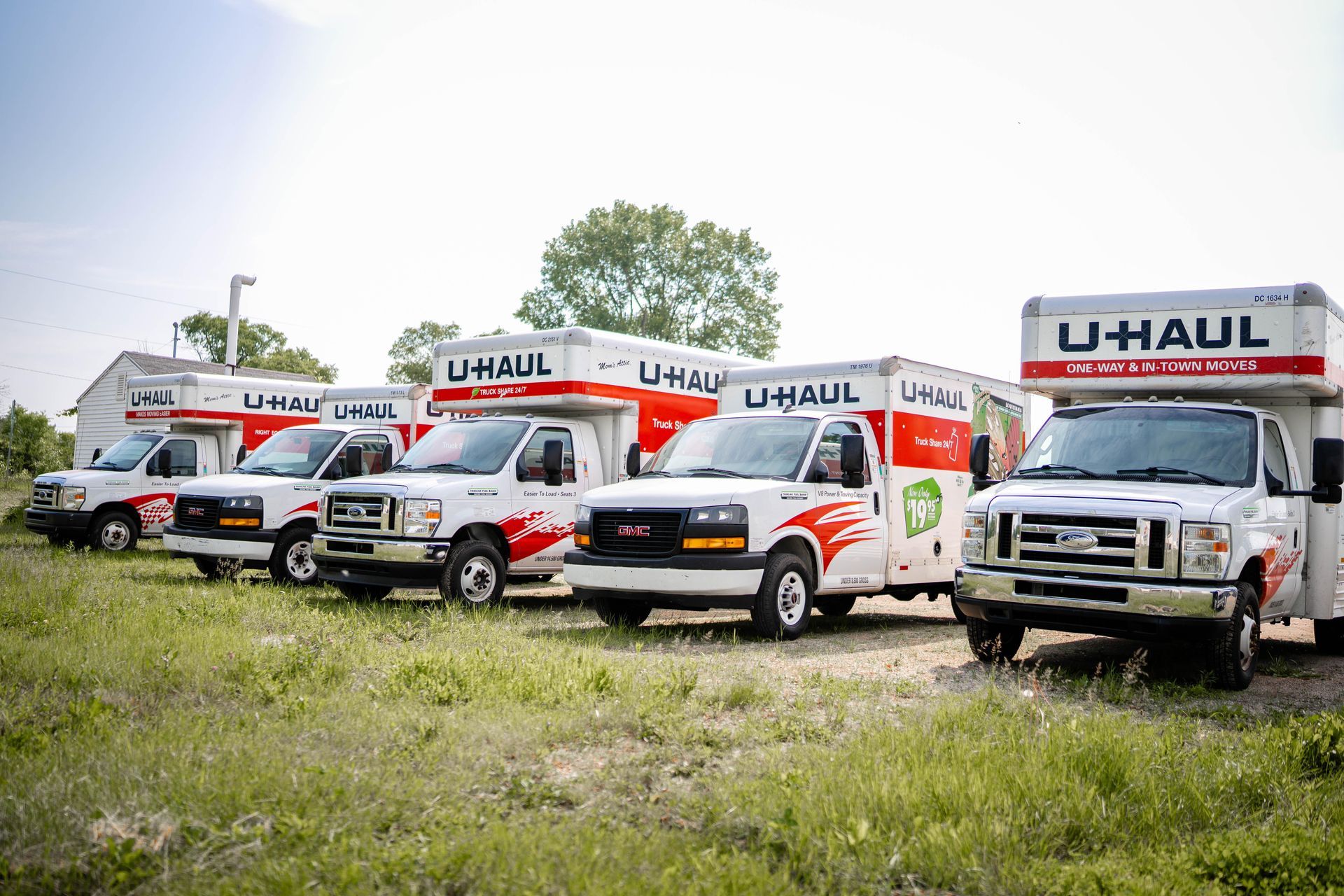 U-Haul moving trucks parked in a row, white with red and green accents, parked on grassy ground.