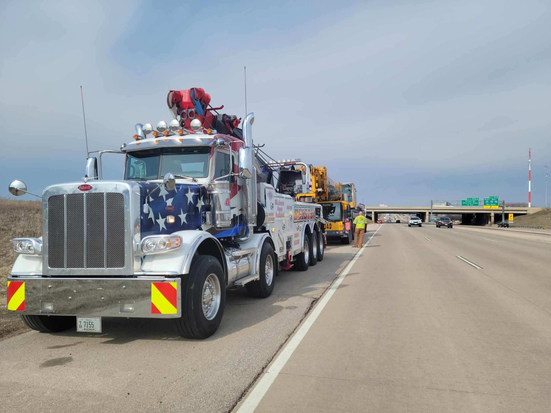 Tow truck convoy parked on a highway shoulder under a cloudy sky