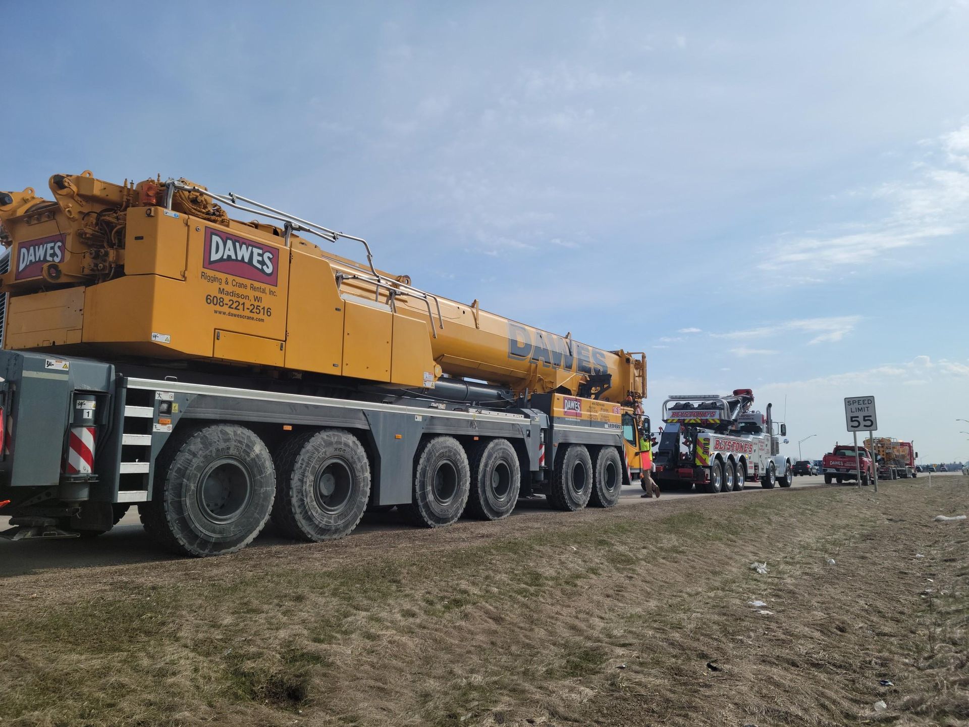 Yellow heavy crane trucks lined up on a muddy field under a cloudy sky