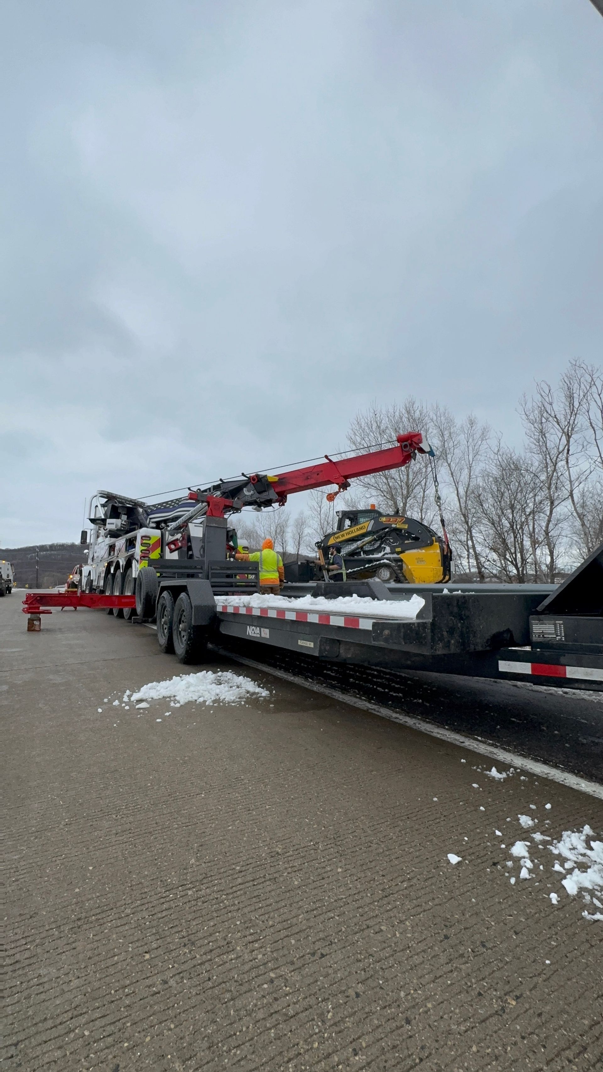 Truck towing flatbed trailer with machinery on snowy road.