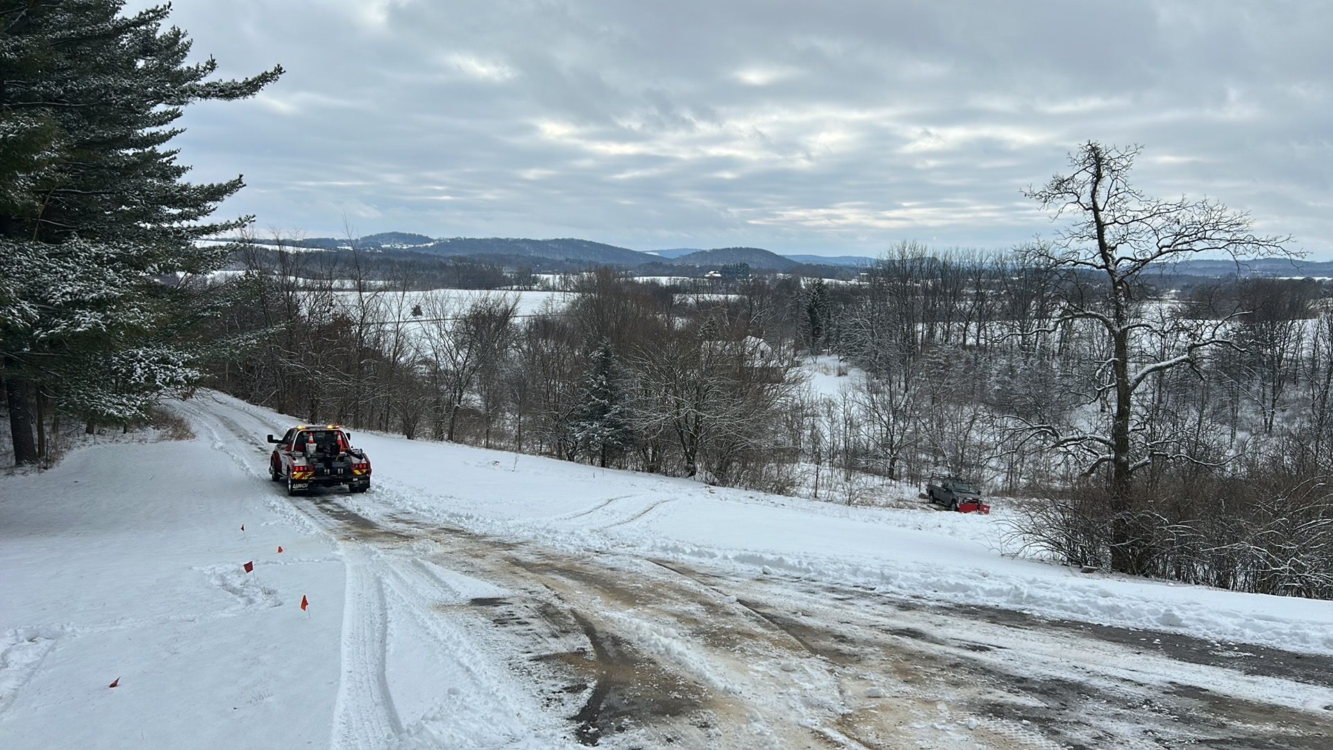 A car drives on a snowy road through a winter landscape with trees and hills.