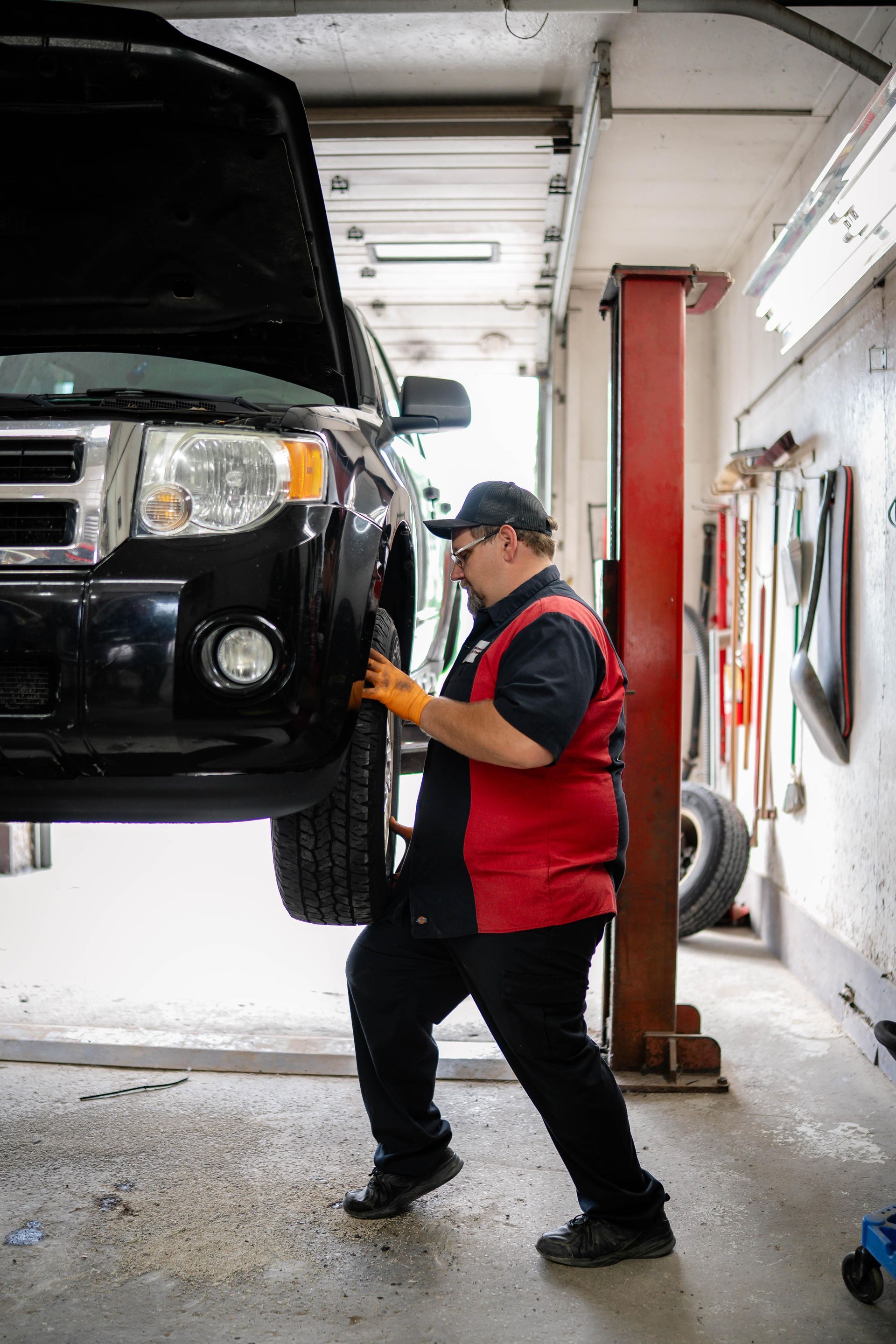 Mechanic in black and red uniform working on a car raised on a lift in a garage.