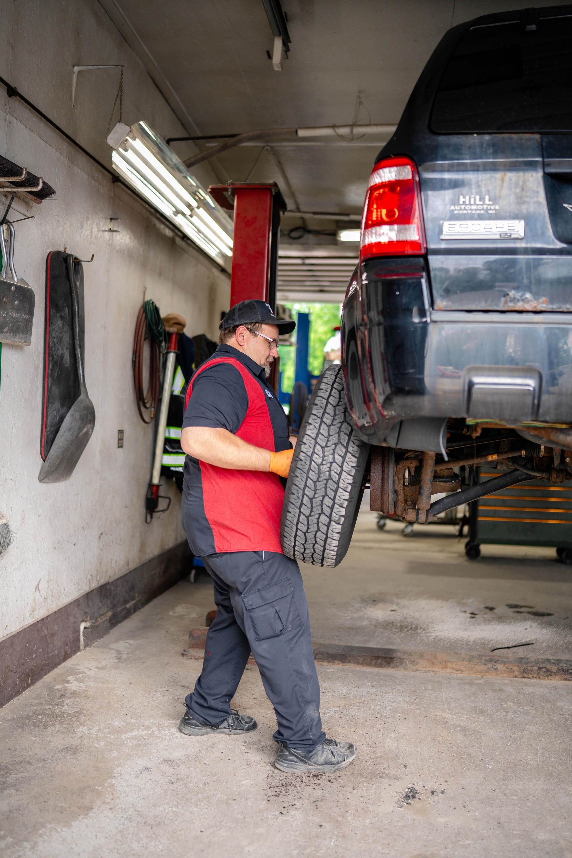 Mechanic holding a tire, lifting it towards a car on a lift in a garage.