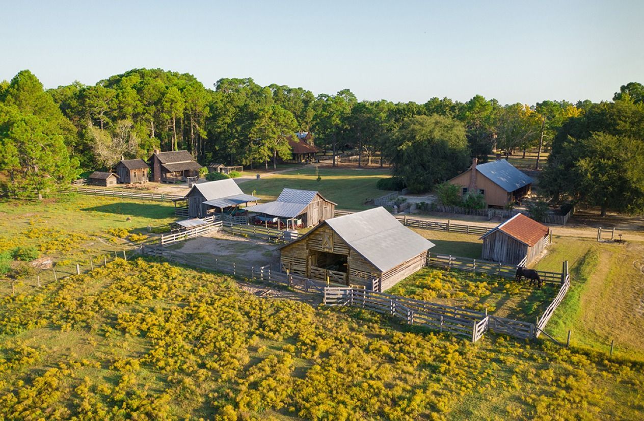 Aerial view of a rural farmstead with barns, a house, and fields surrounded by trees