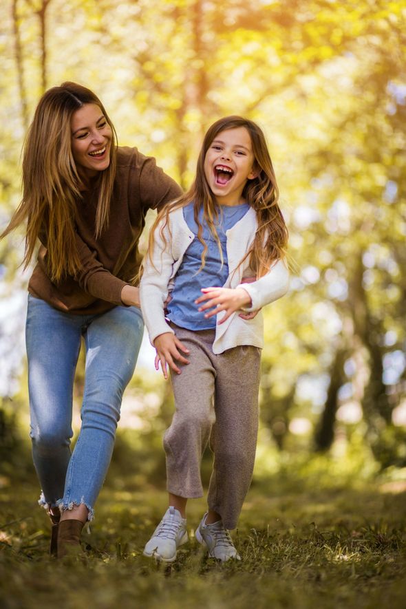 Two people laughing and walking together in a sunny autumn park with yellow trees