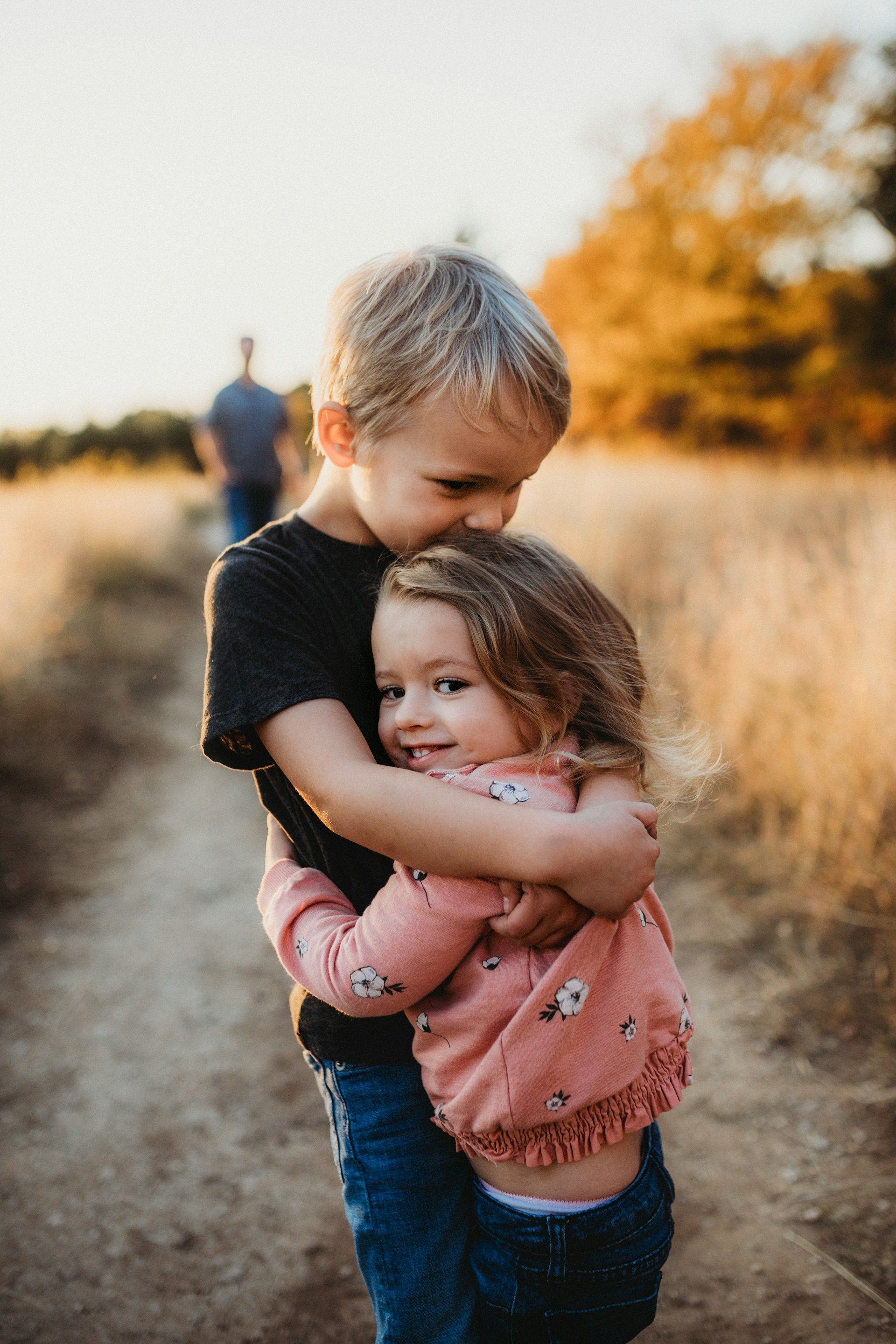 Two children hugging on a dirt path in a golden field at sunset