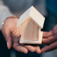 Hands cupping a small wooden house model against a blurred background