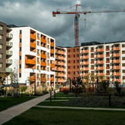 Apartment buildings and a construction crane behind a green courtyard walkway under cloudy skies