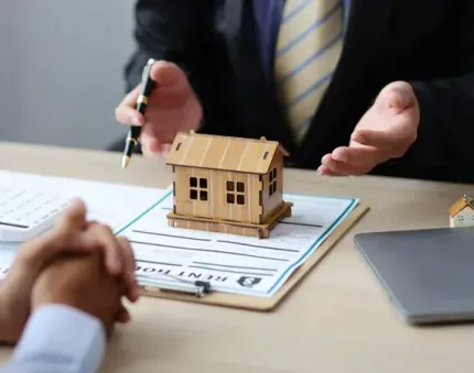 Businesswoman shaking hands across a desk with a laptop and model houses in an office
