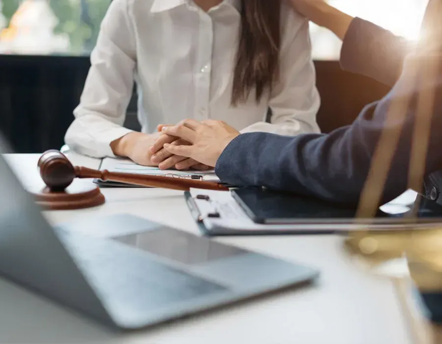 Two people in a business meeting across a desk, with a woman speaking beside a laptop.