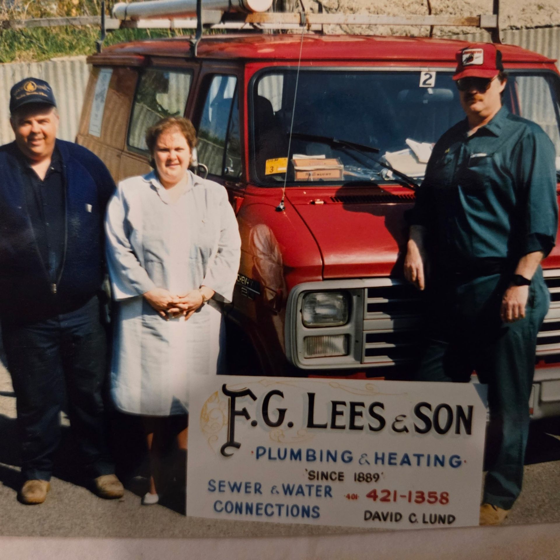 Three people standing beside a red plumbing truck with a F.G. Lees & Son sign