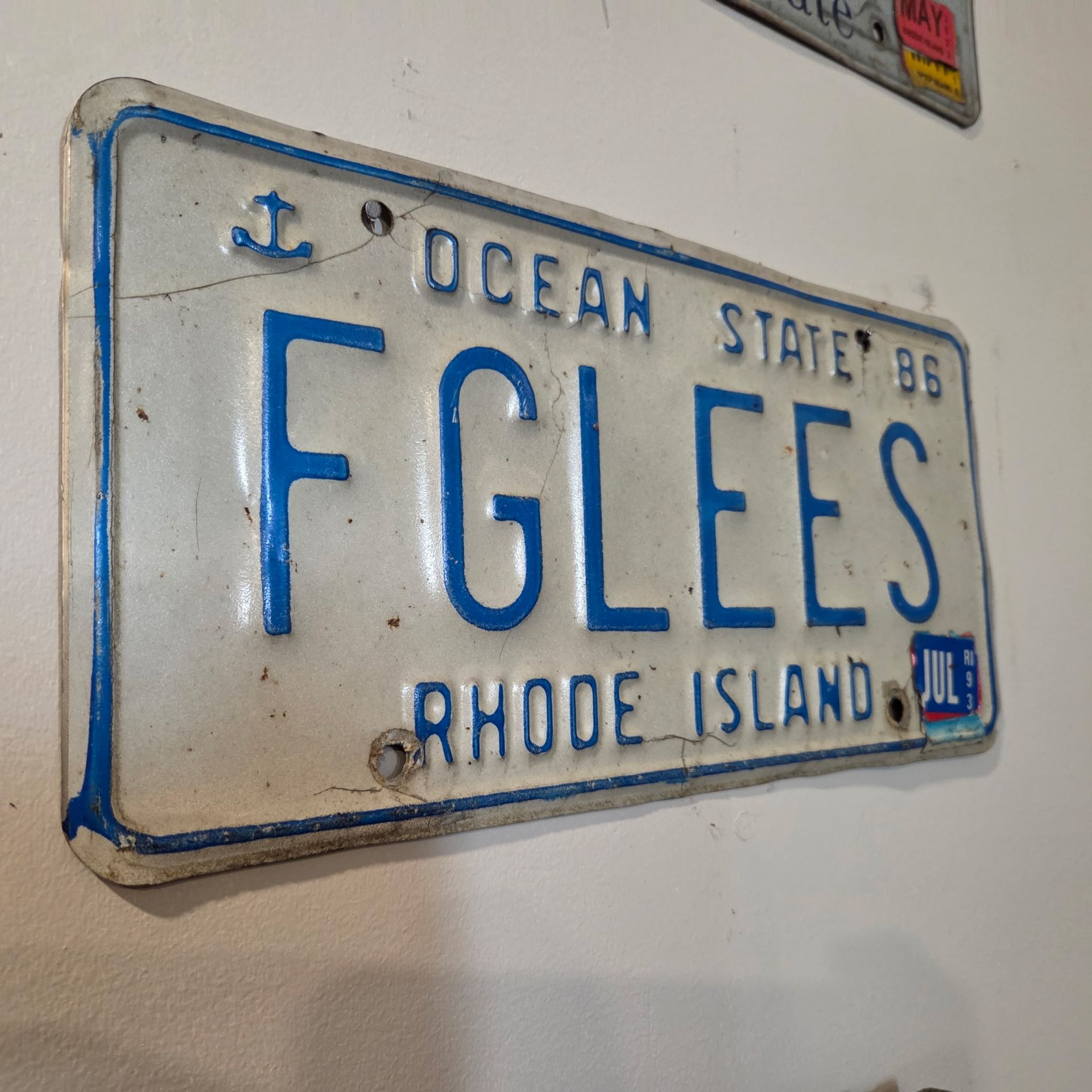 Blue-and-white Rhode Island Ocean State license plate with “FGLEES” on a wall