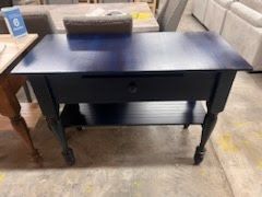 A blue table with a drawer and a shelf is sitting on top of a concrete floor.