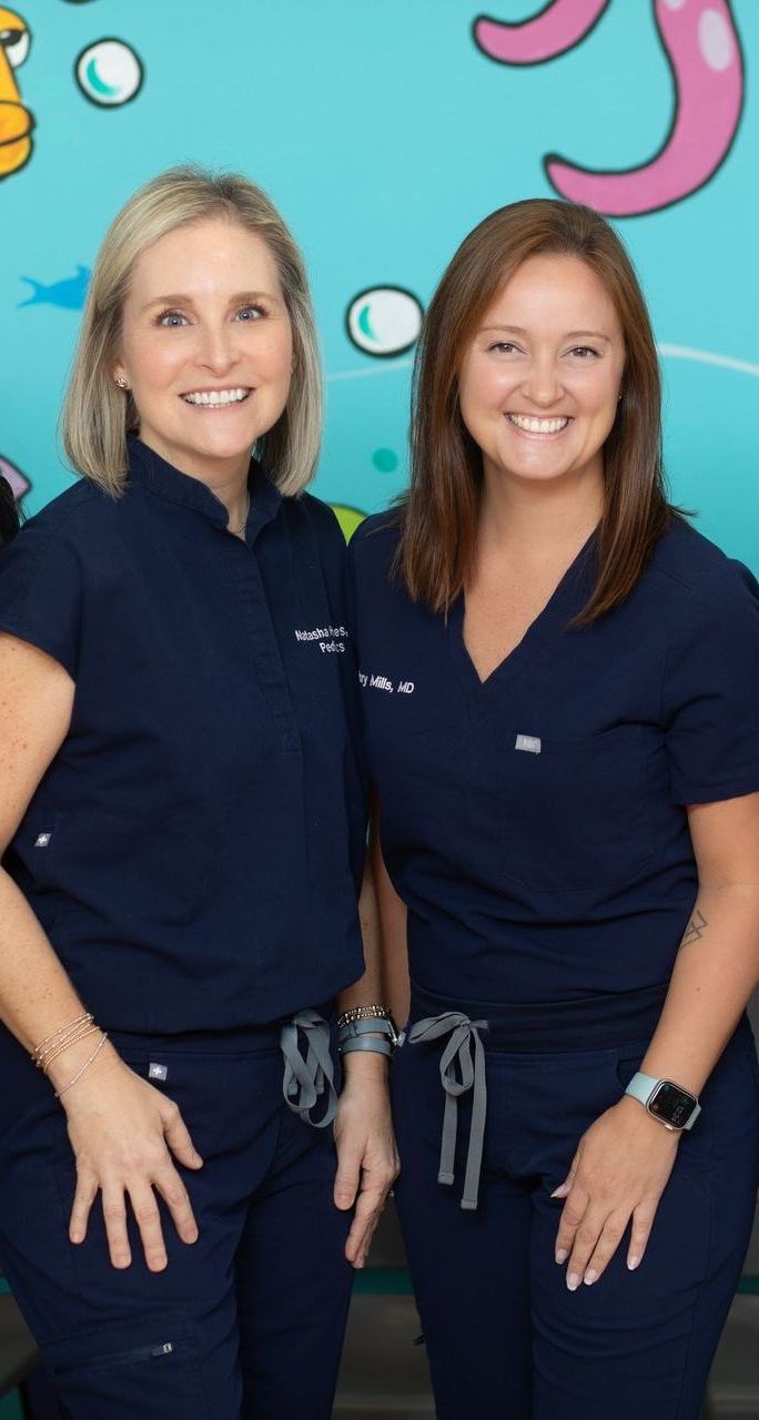 Two women in blue scrubs are posing for a picture.