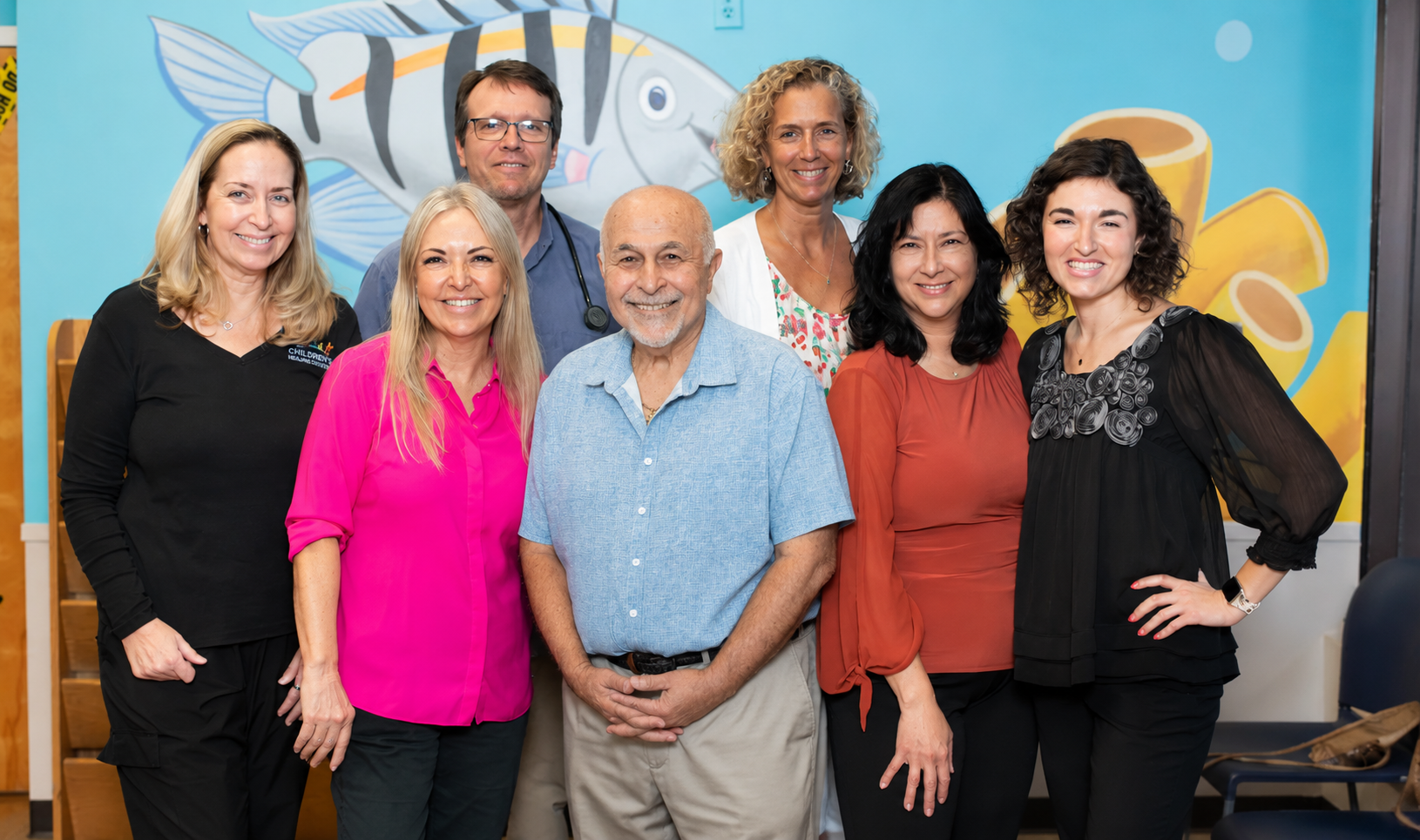 A group of people are posing for a picture in front of a mural of a fish.