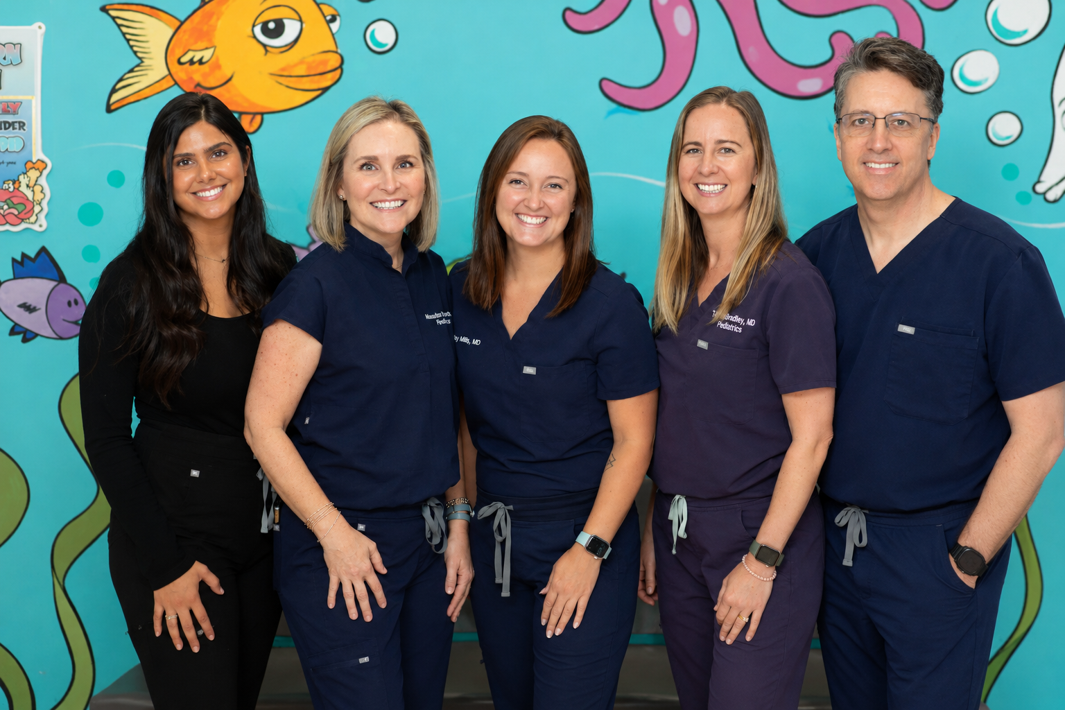 Four women in scrubs are posing for a picture in front of a mural of fish and octopus.