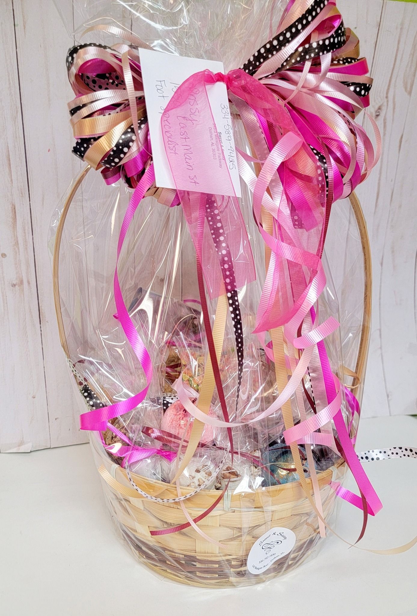 Gift basket wrapped in clear cellophane, with a pink and black bow.