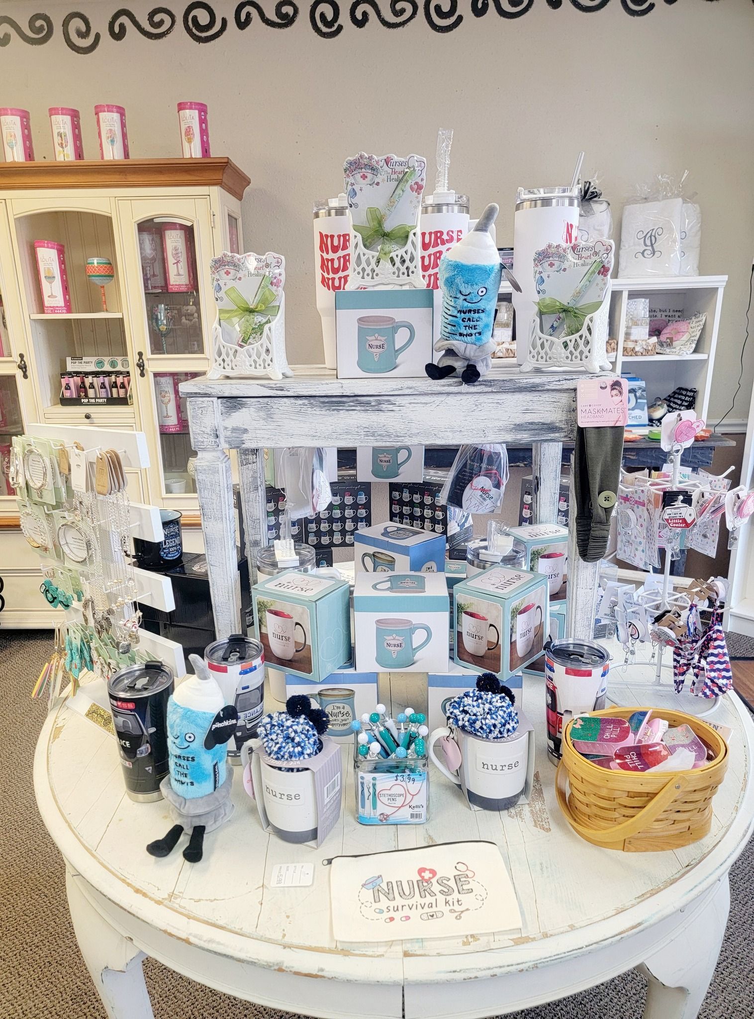 Display of mugs and gifts on a white table in a store with a white cabinet in the background.
