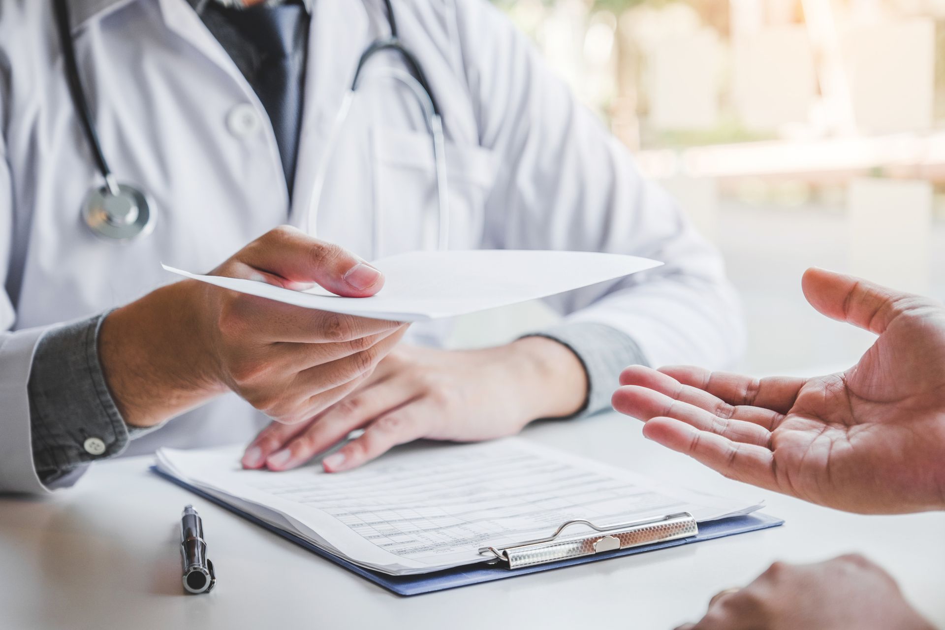 Un médico entrega una receta a un paciente, sentado en un escritorio.