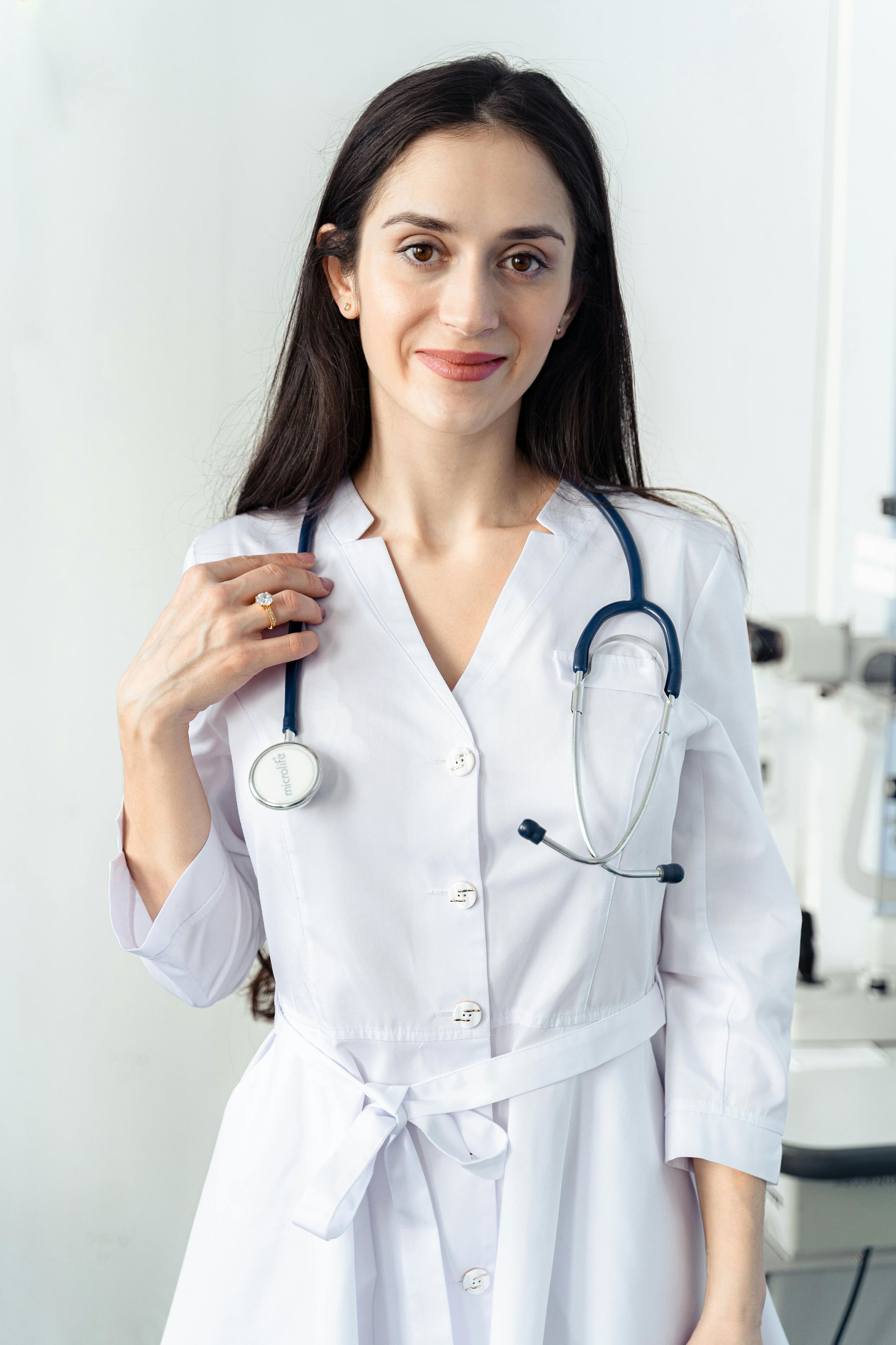 Mujer con bata blanca y estetoscopio, sonriendo, en un entorno médico.