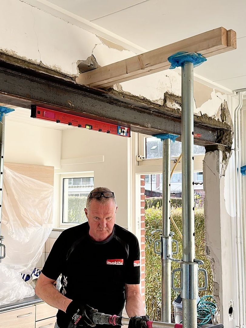 In een kamer staat een man onder een balk van een een betonen draagmuur